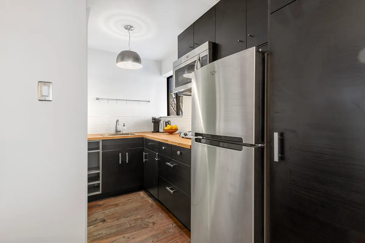 A bright, contemporary kitchenette with a full-size stainless steel refrigerator, wooden countertop, and stylish lighting. The setting is modern and inviting, emphasizing both form and function for cooking or entertaining guests.