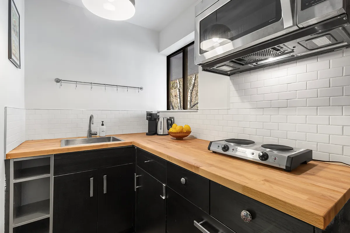 A view of a kitchen area featuring a wooden countertop, modern kitchen appliances, and a decorative fruit bowl. The space appears warm and welcoming, with enough room for preparing meals and socializing. The appliances are compact yet efficient, complementing the overall functional design of the kitchenette.